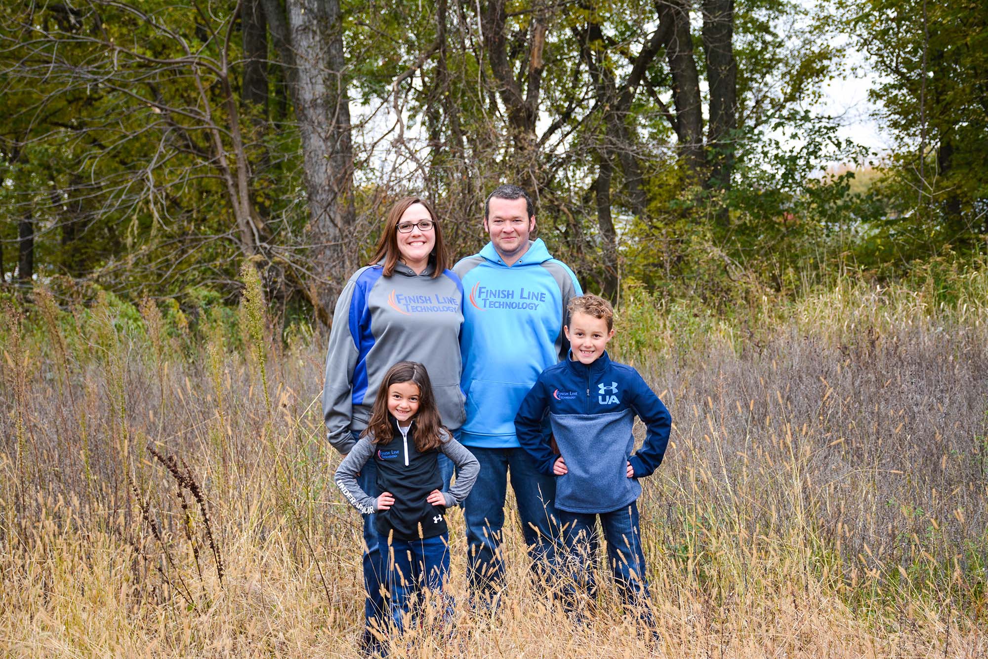 family wearing finish line technology sweatshirts, standing in tall grass